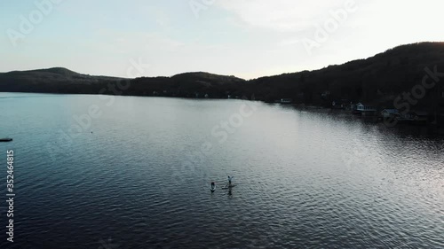 Two Persons Paddleboarding On The Calm Lake In North Hatley, Quebec, Canada On A Sunset - aerial shot photo