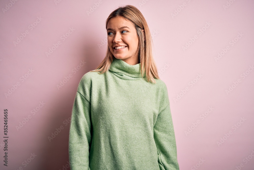 Young beautiful blonde woman wearing winter wool sweater over pink isolated background looking away to side with smile on face, natural expression. Laughing confident. Young beautiful blonde woman wearing winter wool sweater over pink isolated background looking away to side with smile on face, natural expression. Laughing confident.