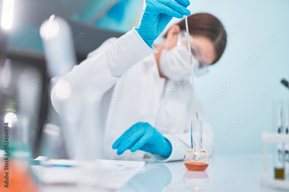 Female lab technician with pipette and flask, blurred background. Female lab technician with pipette and flask, blurred background.