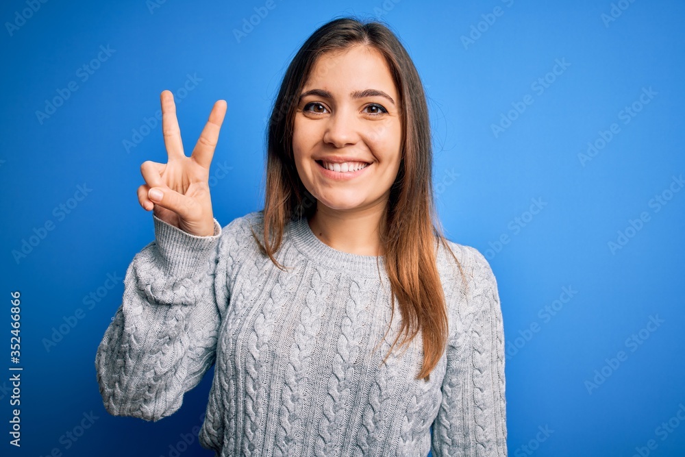 Beautiful young woman wearing casual wool sweater standing over blue isolated background showing and pointing up with fingers number two while smiling confident and happy. Beautiful young woman wearing casual wool sweater standing over blue isolated background showing and pointing up with fingers number two while smiling confident and happy.