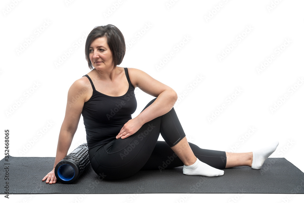 A middle-aged woman, on a gymnastic mat with myofascial roller, is doing a twisting exercise on a white background. A middle-aged woman, on a gymnastic mat with myofascial roller, is doing a twisting exercise on a white background.