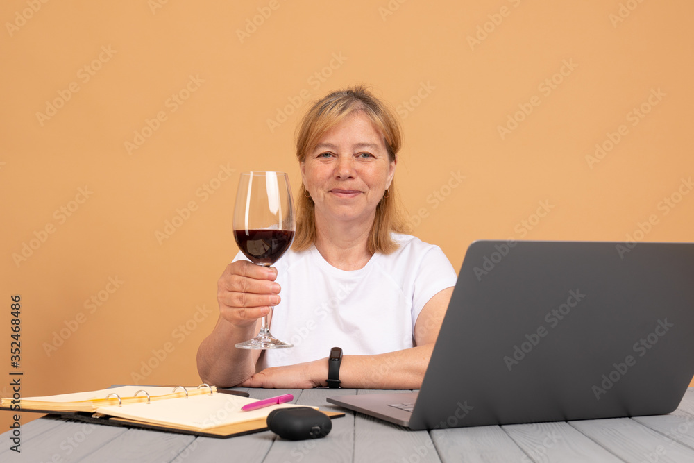 Technology, old age and people concept - happy senior woman in white t-shirt with laptop computer and glass of wine at home Technology, old age and people concept - happy senior woman in white t-shirt with laptop computer and glass of wine at home