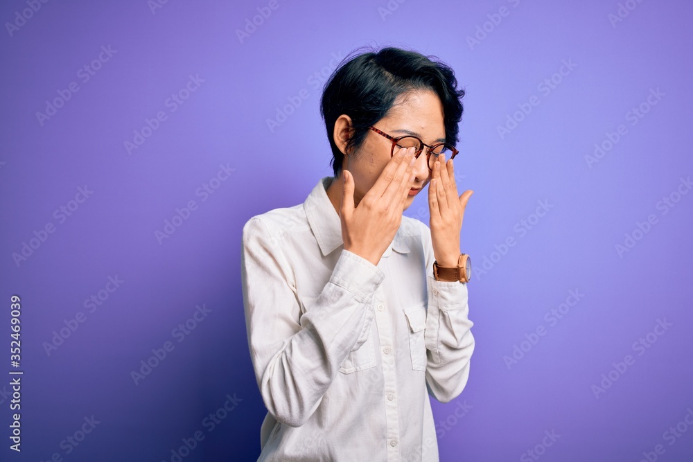 Young beautiful asian girl wearing casual shirt and glasses standing over purple background rubbing eyes for fatigue and headache, sleepy and tired expression. Vision problem Young beautiful asian girl wearing casual shirt and glasses standing over purple background rubbing eyes for fatigue and headache, sleepy and tired expression. Vision problem