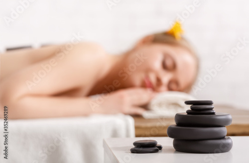 Pile of massage stones for spa, close up. Girl with hot stones on back, soft background