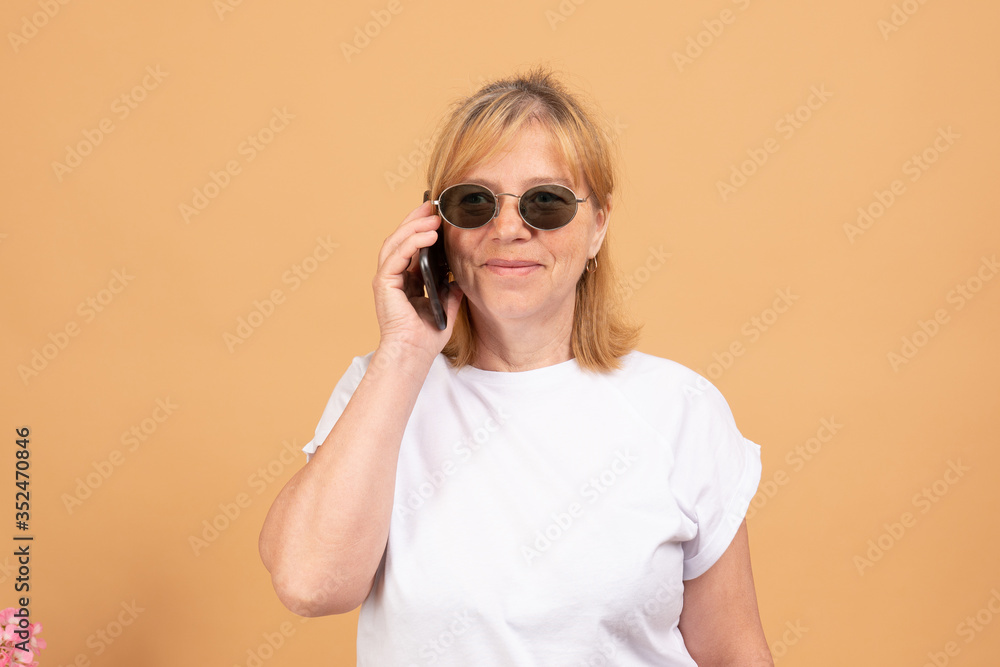 Phone conversation. Positive aged woman in black sunglasses smiling while talking on the phone Phone conversation. Positive aged woman in black sunglasses smiling while talking on the phone