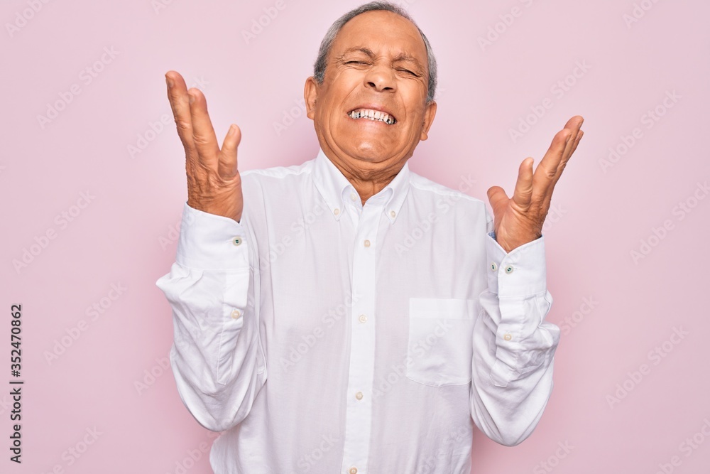 Senior handsome grey-haired man wearing elegant shirt over isolated pink background celebrating mad and crazy for success with arms raised and closed eyes screaming excited. Winner concept Senior handsome grey-haired man wearing elegant shirt over isolated pink background celebrating mad and crazy for success with arms raised and closed eyes screaming excited. Winner concept