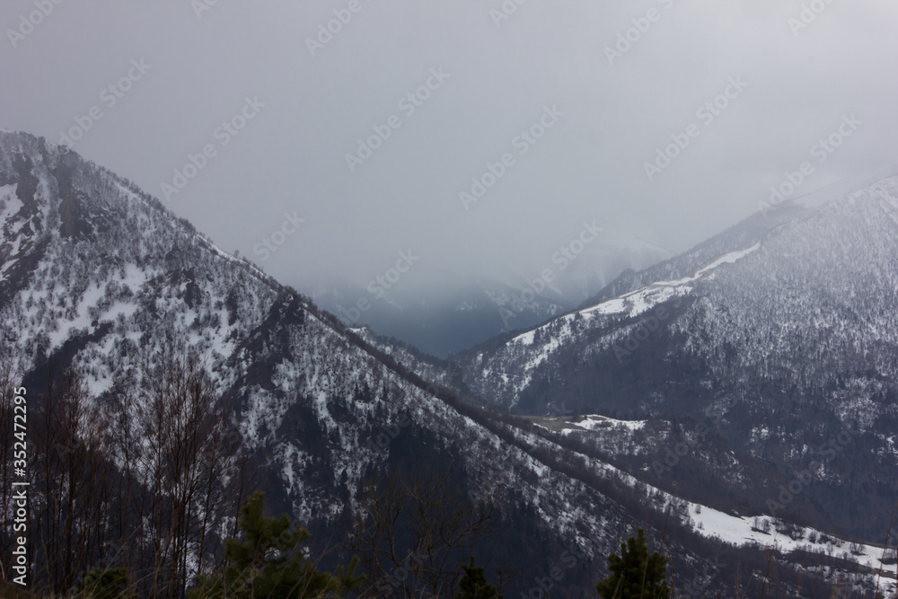Snow-capped mountains in the fog. Caucasian ridge at the beginning of winter. The first snow in the mountains of Russia.