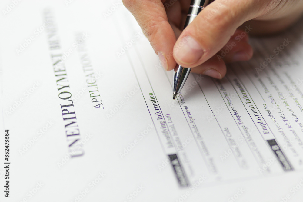 Close-up of a person's hand filing social security benefits application form. Concept of Covid-19 coronavirus and stay at home order impact on economy, world economic crisis, unemployment. Close-up of a person's hand filing social security benefits application form. Concept of Covid-19 coronavirus and stay at home order impact on economy, world economic crisis, unemployment.