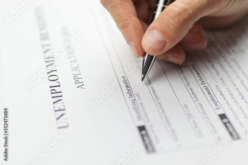Close-up of a person's hand filing social security benefits application form. Concept of Covid-19 coronavirus and stay at home order impact on economy, world economic crisis, unemployment.
