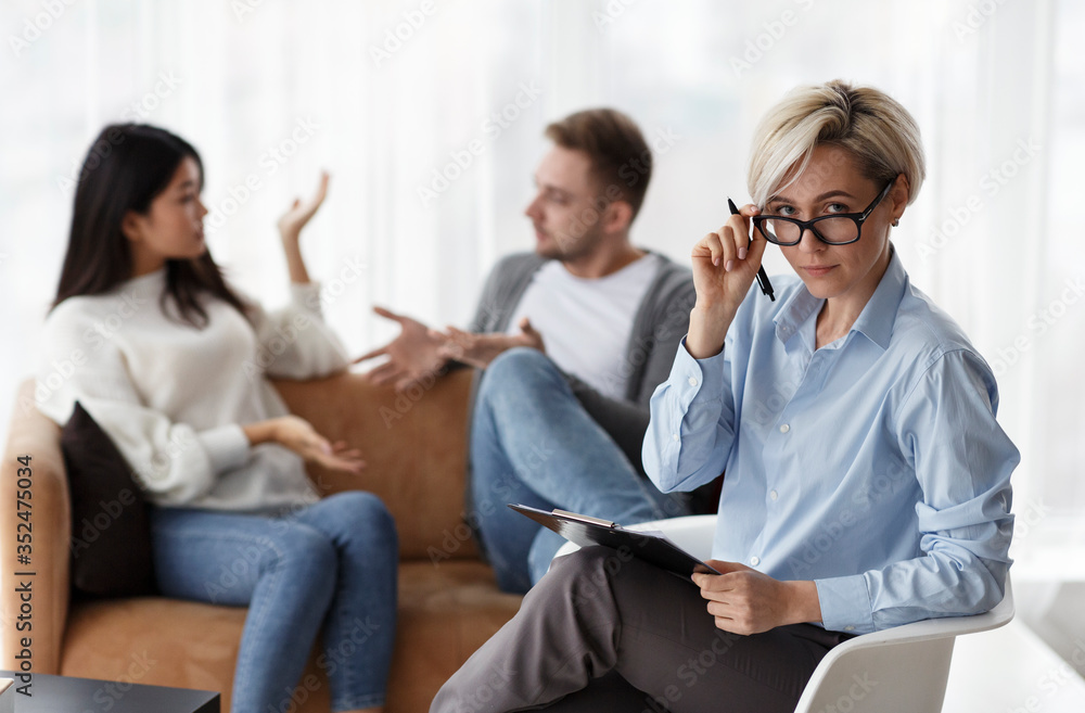 Psychologist Looking At Camera While Clients Having Quarrel In Office