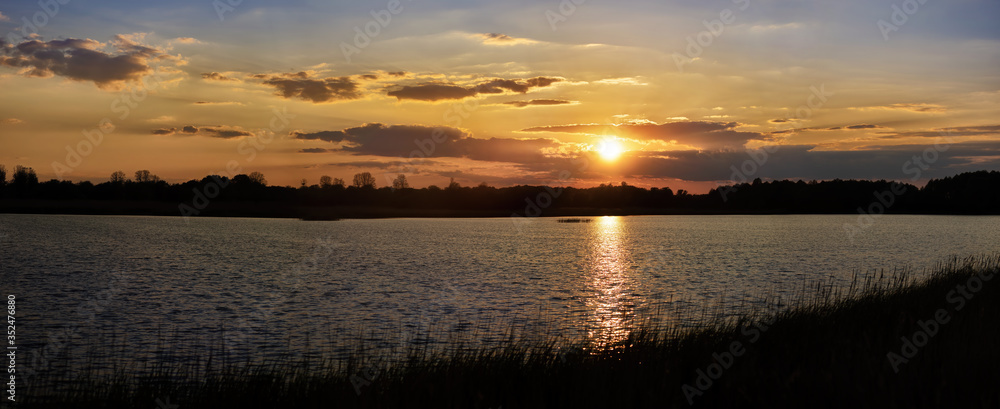 Panoramic photo of beautiful sunset with blue sky trees and water in the foreground