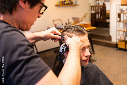 Barber trims the hair of young man with a razor