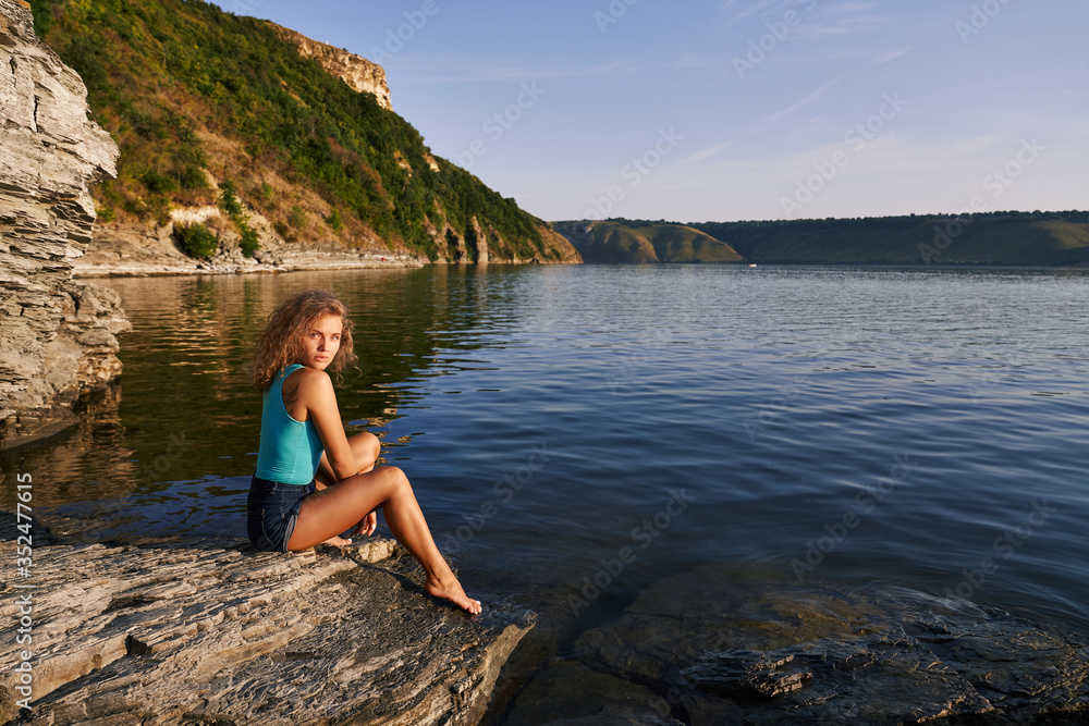 Pretty girl sitting on shore of lake.