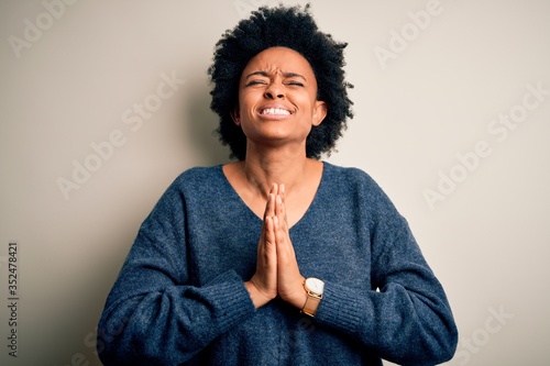 Young beautiful African American afro woman with curly hair wearing casual sweater begging and praying with hands together with hope expression on face very emotional and worried. Begging. © Krakenimages.com