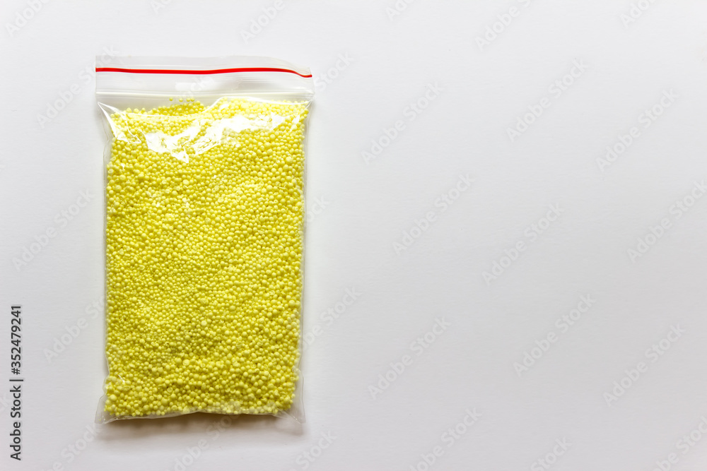 Granules of yellow sulfur chemical element in a plastic bag on white background. Photo with copy blank space.