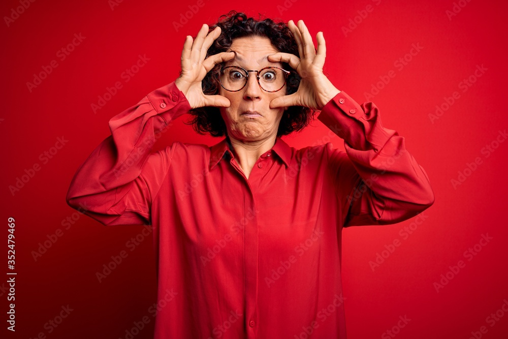 Middle age beautiful curly hair woman wearing casual shirt and glasses over red background Trying to open eyes with fingers, sleepy and tired for morning fatigue
