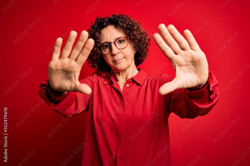 Middle age beautiful curly hair woman wearing casual shirt and glasses over red background doing frame using hands palms and fingers, camera perspective Middle age beautiful curly hair woman wearing casual shirt and glasses over red background doing frame using hands palms and fingers, camera perspective