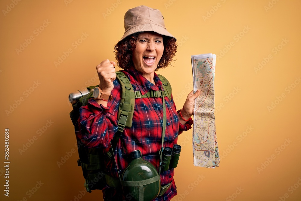 Middle age curly hair hiker woman hiking wearing backpack and water canteen holding city map screaming proud and celebrating victory and success very excited, cheering emotion