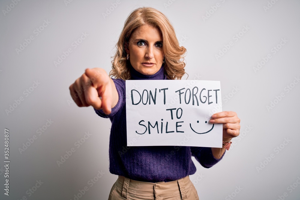 Middle age beautiful blonde woman holding banner funny positive message pointing with finger to the camera and to you, hand sign, positive and confident gesture from the front Middle age beautiful blonde woman holding banner funny positive message pointing with finger to the camera and to you, hand sign, positive and confident gesture from the front
