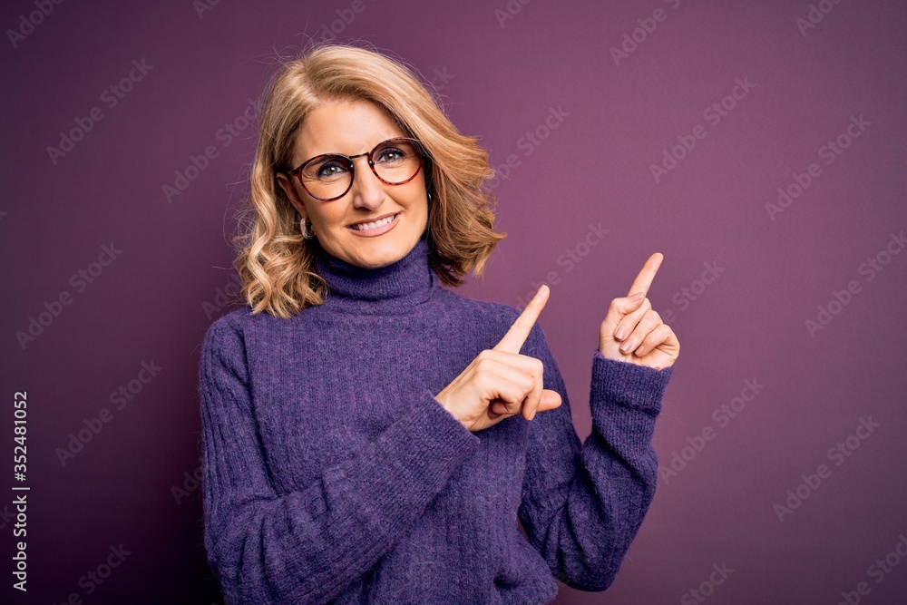 Middle age beautiful blonde woman wearing casual purple turtleneck sweater and glasses smiling and looking at the camera pointing with two hands and fingers to the side. Middle age beautiful blonde woman wearing casual purple turtleneck sweater and glasses smiling and looking at the camera pointing with two hands and fingers to the side.