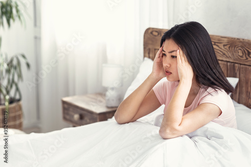 Asian Girl Having Migraine Pain Sitting In Bed At Home