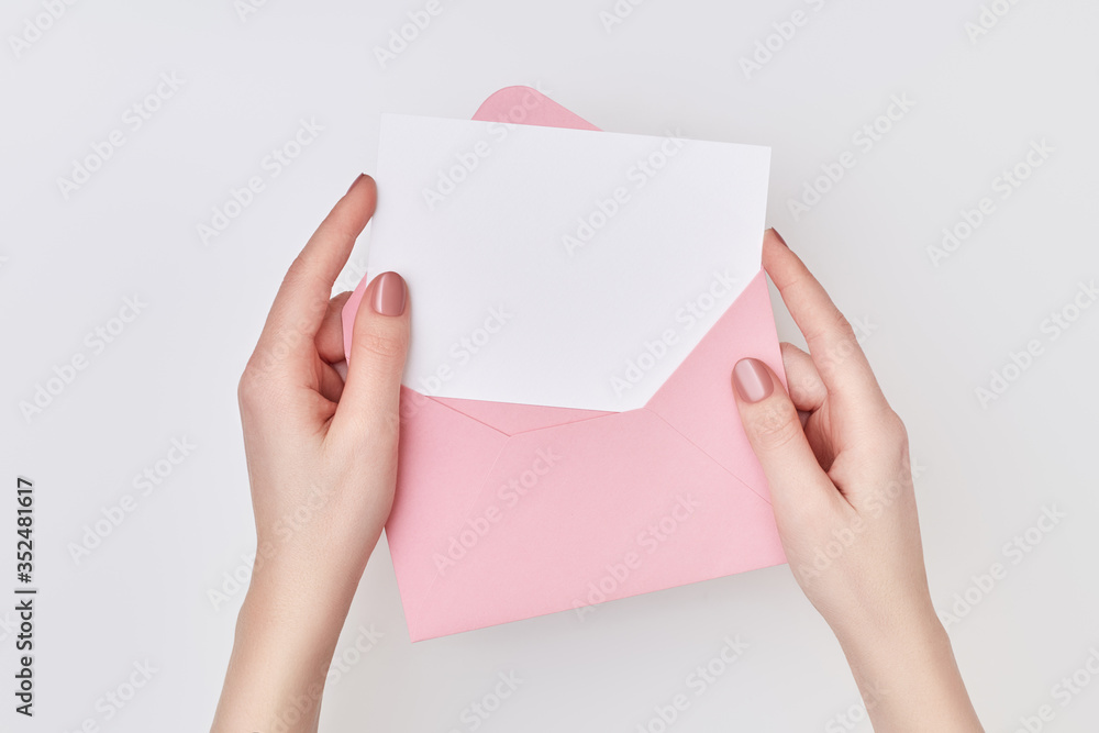 Pink envelope with blank white postcard in woman's hands on the white background. Mail concept Pink envelope with blank white postcard in woman's hands on the white background. Mail concept