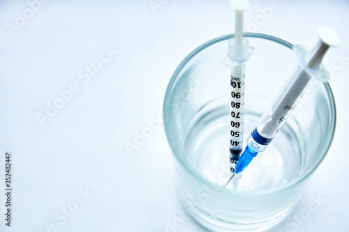 Two syringes put in a glass on a white background. Top view, close-up.