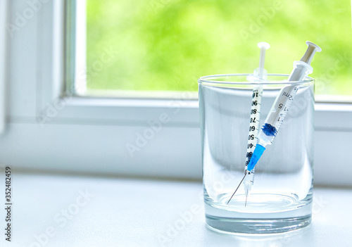 Two syringes put in a glass on a windowsill with window background, copy space. 