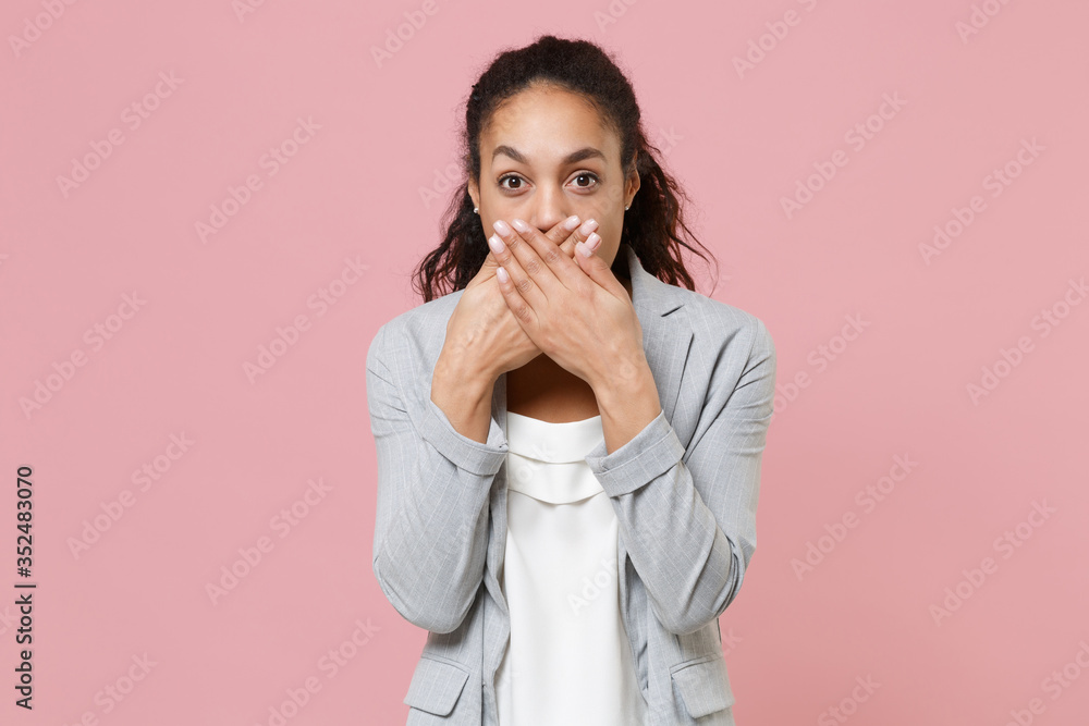 Shocked young african american business woman in grey suit white shirt posing isolated on pink wall background studio portrait. Achievement career wealth business concept. Covering mouth with hands. Shocked young african american business woman in grey suit white shirt posing isolated on pink wall background studio portrait. Achievement career wealth business concept. Covering mouth with hands.