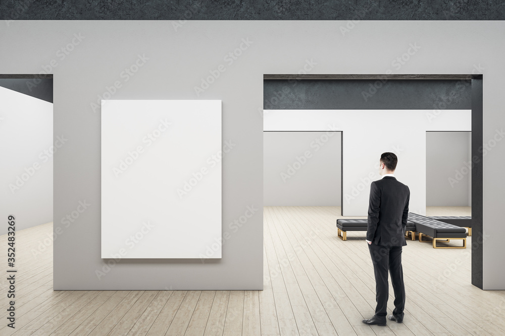 Fototapeta premium Businessman looking on blank billboard in minimalistic gallery interior.