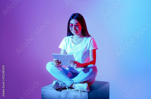 New generation. Millennial girl in round glasses sits with legs folded with tablet photo