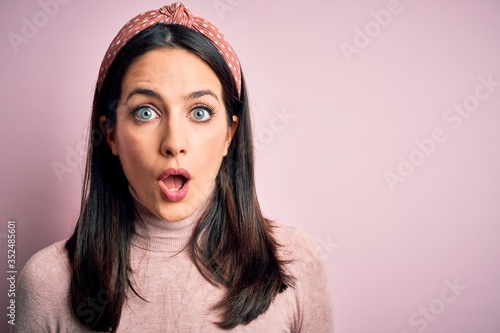 Young brunette woman with blue eyes wearing casual t-shirt and diadem afraid and shocked with surprise expression, fear and excited face.