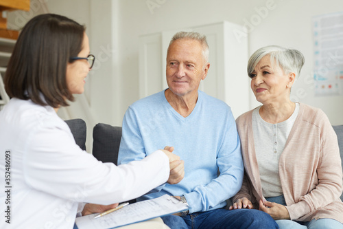 Portrait of smiling senior couple shaking hands with female doctor while visiting private clinic