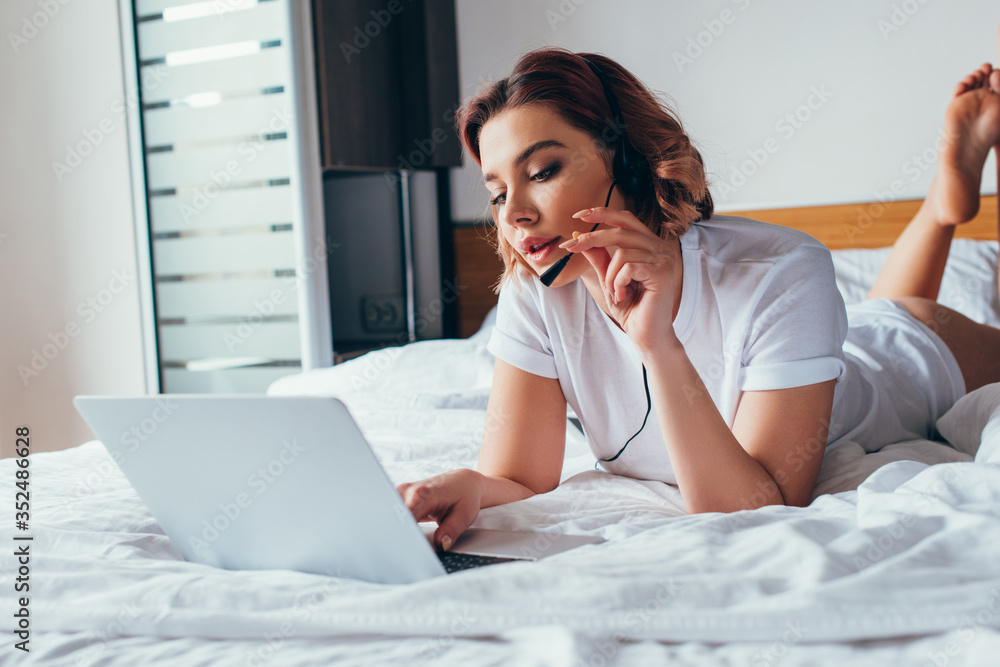 attractive girl making video call with headset and laptop in bed during self isolation attractive girl making video call with headset and laptop in bed during self isolation