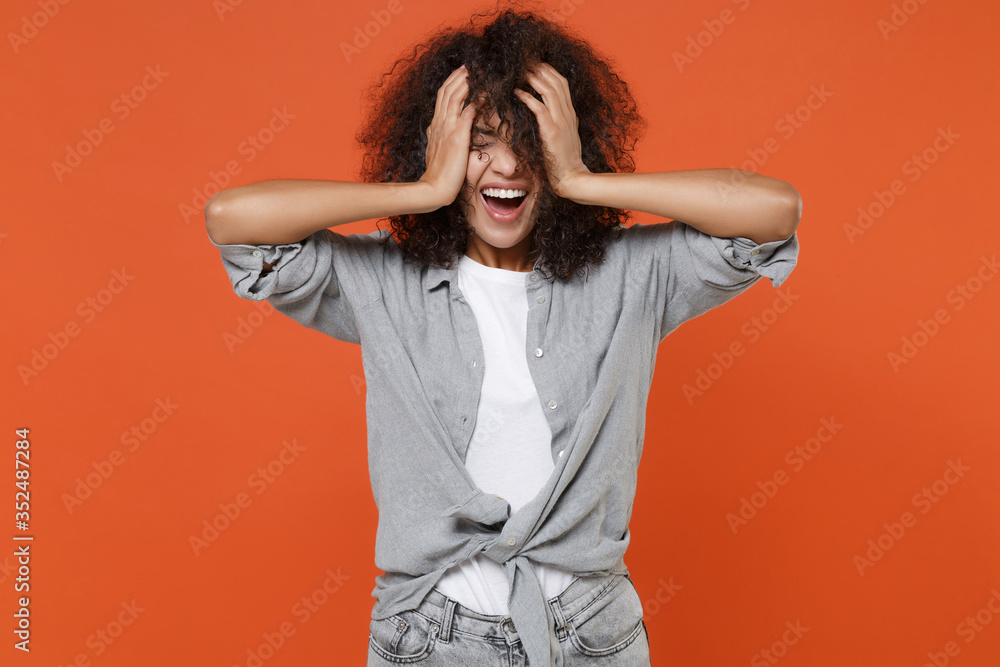 Cheerful young african american woman girl in gray casual clothes isolated on orange background studio portrait. People lifestyle concept. Mock up copy space. Keeping eyes closed, put hands on head. Cheerful young african american woman girl in gray casual clothes isolated on orange background studio portrait. People lifestyle concept. Mock up copy space. Keeping eyes closed, put hands on head.