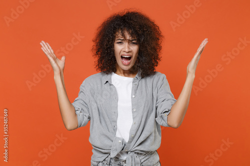 Irritated young african american woman girl in gray casual clothes posing isolated on orange background in studio. People lifestyle concept. Mock up copy space. Screaming swearing spreading hands.