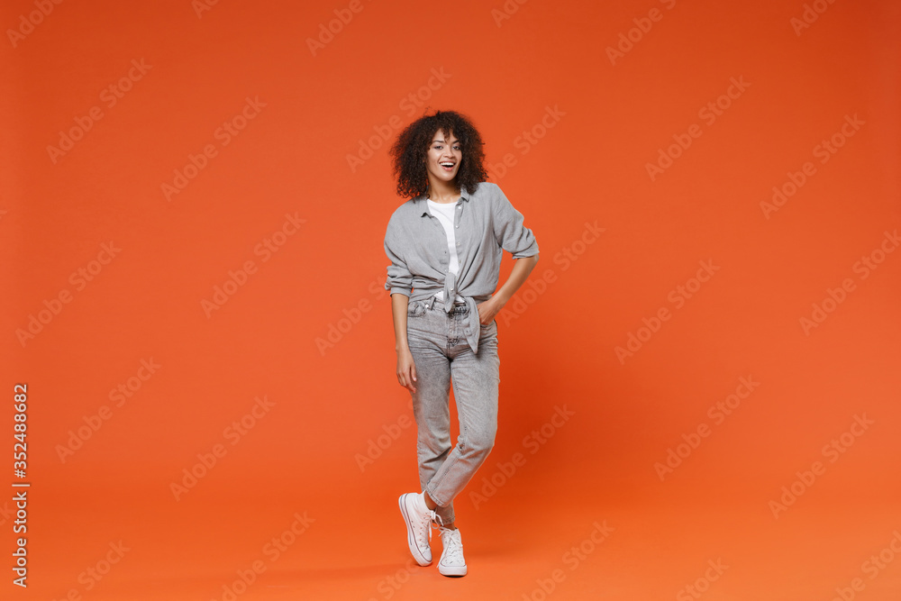 Cheerful young african american woman girl in gray casual clothes posing isolated on orange background studio portrait. People sincere emotions lifestyle concept. Mock up copy space. Looking camera.