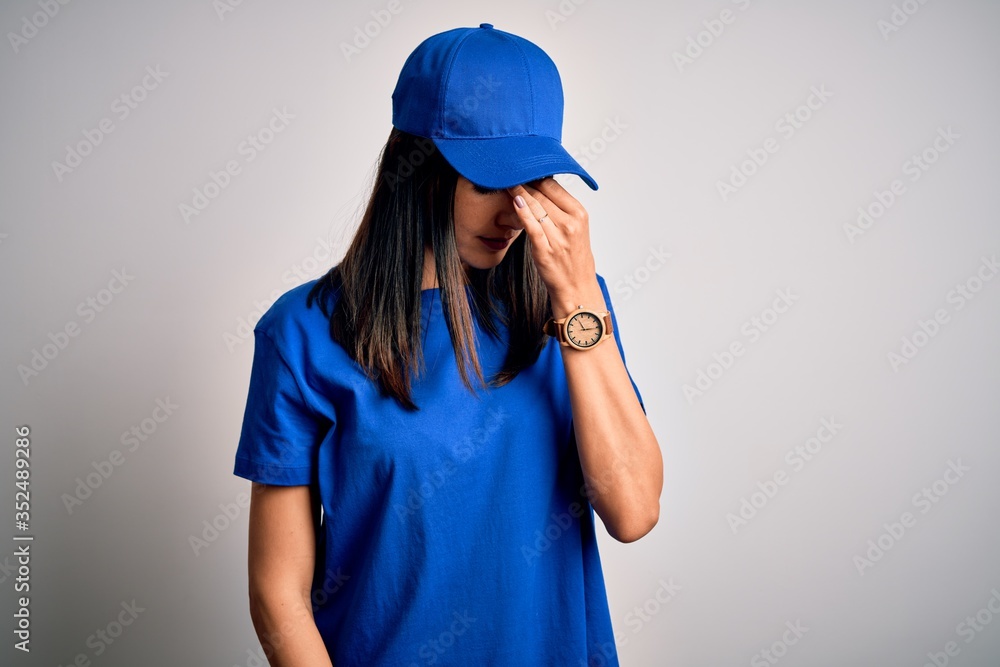 Young delivery woman with blue eyes wearing cap standing over blue background tired rubbing nose and eyes feeling fatigue and headache. Stress and frustration concept.