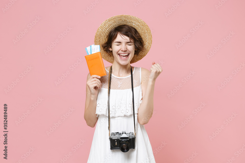 Happy young tourist girl in summer dress hat with photo camera isolated on pink background. Traveling abroad weekend getaway. Air flight journey concept. Hold passport tickets doing winner gesture. Happy young tourist girl in summer dress hat with photo camera isolated on pink background. Traveling abroad weekend getaway. Air flight journey concept. Hold passport tickets doing winner gesture.