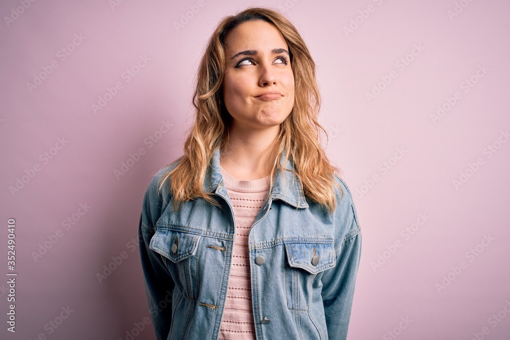 Young beautiful blonde woman wearing casual denim jacket standing over pink background smiling looking to the side and staring away thinking. Young beautiful blonde woman wearing casual denim jacket standing over pink background smiling looking to the side and staring away thinking.