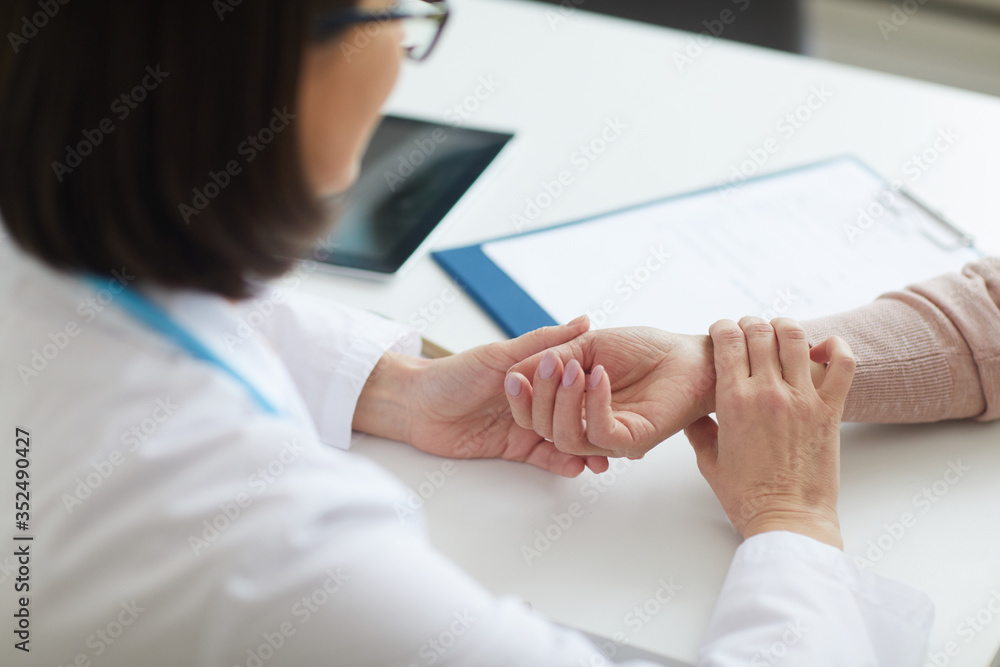 High angle view at female doctor checking heart rate of unrecognizable senior patient and holding wrist during consultation in clinic, copy space High angle view at female doctor checking heart rate of unrecognizable senior patient and holding wrist during consultation in clinic, copy space