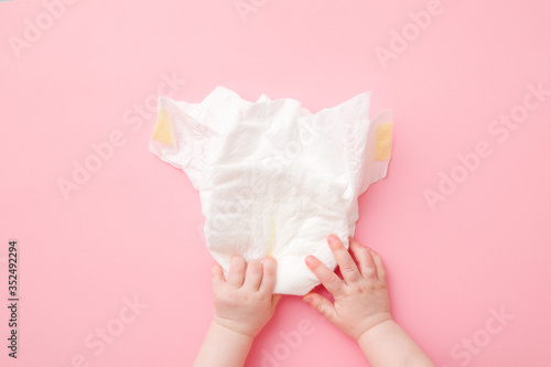 Tableau sur toile Baby hands touching white diaper on light pink table background