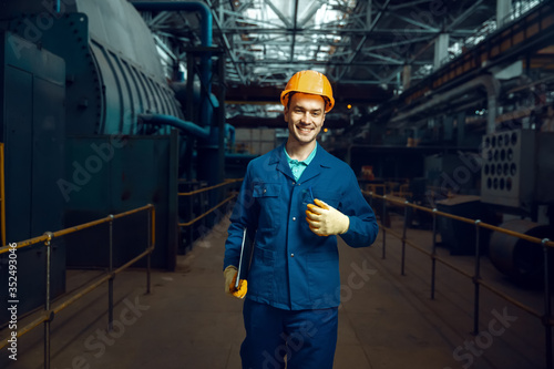 Smiling worker holds notebook, factory floor