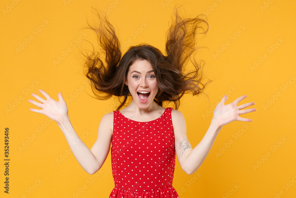 Excited young brunette woman girl in red summer dress posing isolated on yellow wall background studio portrait. People lifestyle concept. Mock up copy space. Spreading hands, throwing flying hair. Excited young brunette woman girl in red summer dress posing isolated on yellow wall background studio portrait. People lifestyle concept. Mock up copy space. Spreading hands, throwing flying hair.