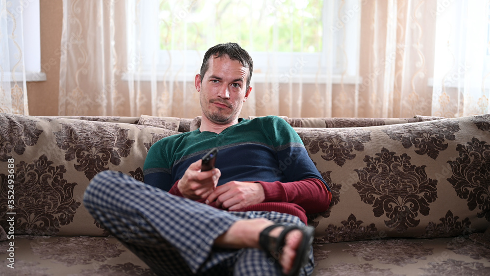 Displeased man sitting on a sofa with a TV remote