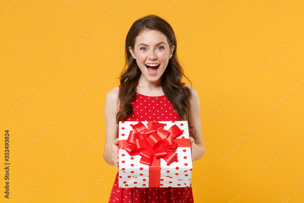 Excited young woman girl in red summer dress posing isolated on yellow wall background studio portrait. Birthday holiday concept. Mock up copy space. Hold white red present box with gift ribbon bow. Excited young woman girl in red summer dress posing isolated on yellow wall background studio portrait. Birthday holiday concept. Mock up copy space. Hold white red present box with gift ribbon bow.