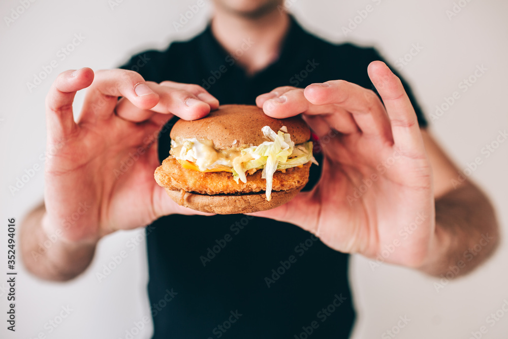 Young man isolated over white background. Cut view of guy holding tasty delicious cheeseburger in hands. Fast food and unhealthy meal. Meat between two rolls.