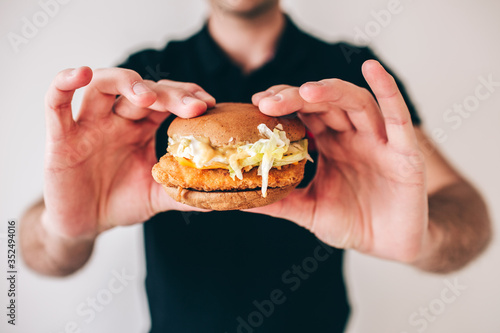 Young man isolated over white background. Cut view of guy holding tasty delicious cheeseburger in hands. Fast food and unhealthy meal. Meat between two rolls.