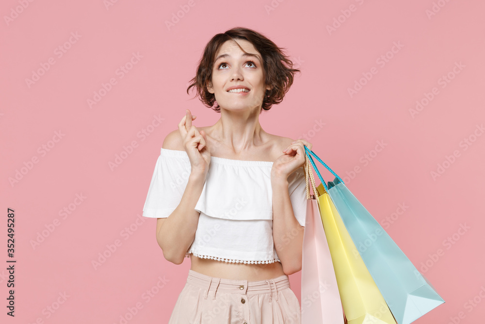 Pensive woman in summer clothes hold package bag with purchases isolated on pink background. Shopping discount sale concept. Wait for special moment, keeping fingers crossed, biting lips, making wish. Pensive woman in summer clothes hold package bag with purchases isolated on pink background. Shopping discount sale concept. Wait for special moment, keeping fingers crossed, biting lips, making wish.