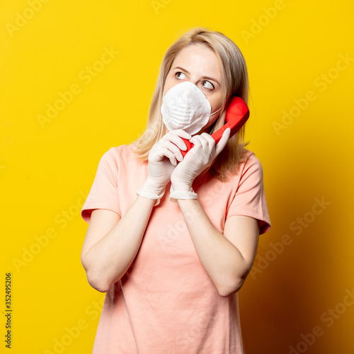 Blonde girl in face mask and pink dress holding a handser on yellow background.